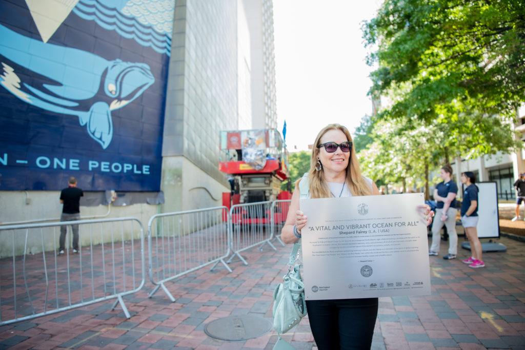Linda Cabot holds the plaque for Shepard Fairey's mural "A Vital and Vibrant Ocean for All."