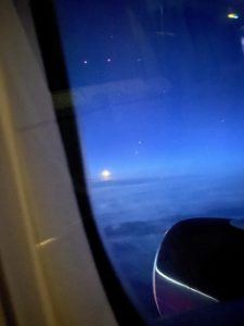 A view of a blue sky with the moon and stars outside of an airplane window.