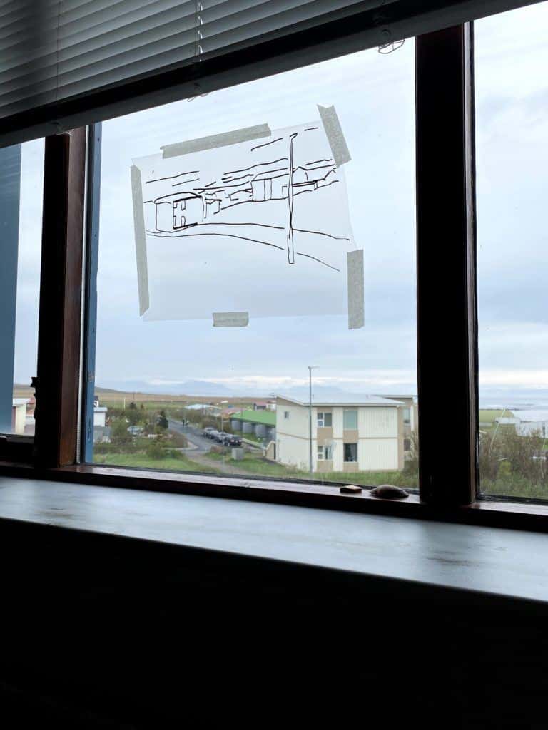 A view out of a window with a taped drawing over it of the buildings beyond it.