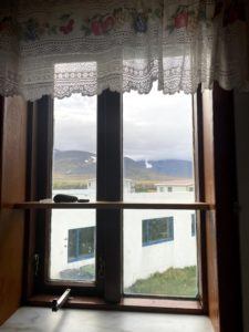 A picture of a view of the mountains and white buildings from out a paneled window with a lace fringe out the top.