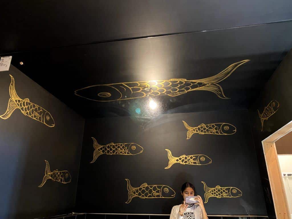 A mirror-selfie of Ely standing in the black bathroom she painted with a golden fish pattern.