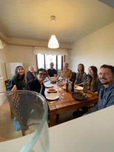 A picture of Ely and the other NES residents sitting at the dining table together, smiling as they all look towards the camera.