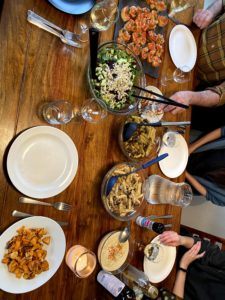 A picture taken from above of a meel of pasta salad, green salad, potatoes, and bruschetta on a wooden table, with some of the residents' hands in view.