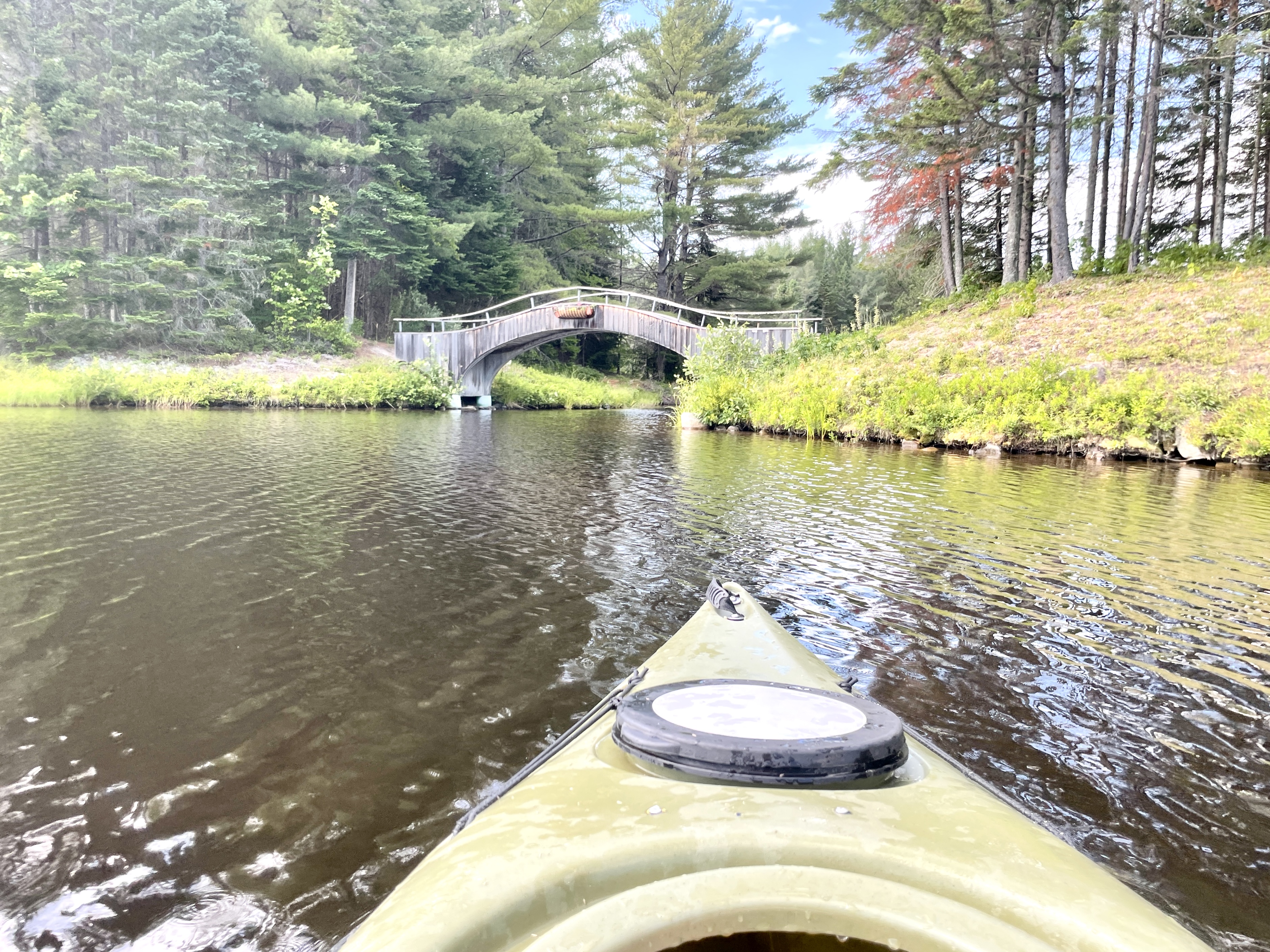 Kayak in a river in New Hampshire, facing a foot bridge.