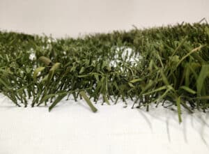 Close-up of artificial grass blades on a white surface, showcasing varying shades of green and texture.