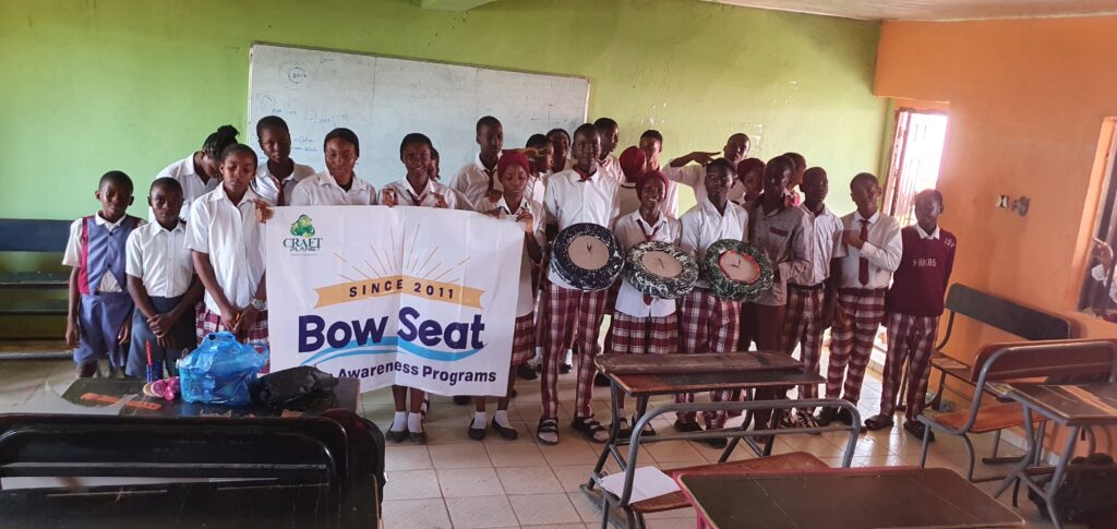 A group of students in a classroom hold a banner that reads "Bow Seat Awareness Programs" and display their artwork.