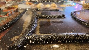 Close-up of a shiny, textured surface with black raised lettering and scattered stones in the background.