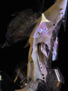 Close-up of an abstract sculpture with transparent, irregular shapes adorned with metallic rivets against a black background.