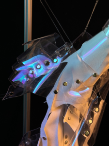 Close-up of an art installation featuring translucent plastic sheets with metallic eyelets and reflective lighting against a dark background.