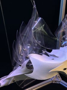 Abstract art installation featuring layered transparent and white materials with small black accents on a structural frame.